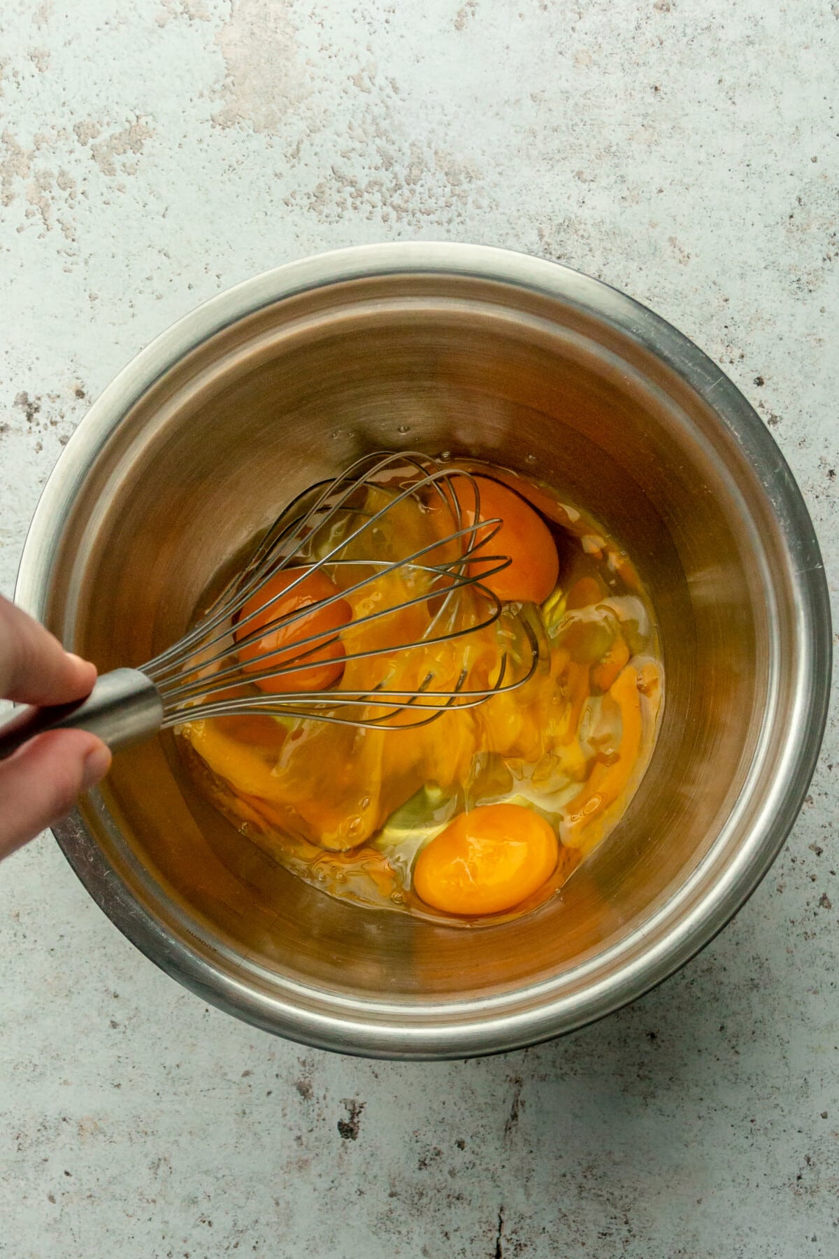 Eggs are whisked in a stainless steel bowl on a light gray surface.