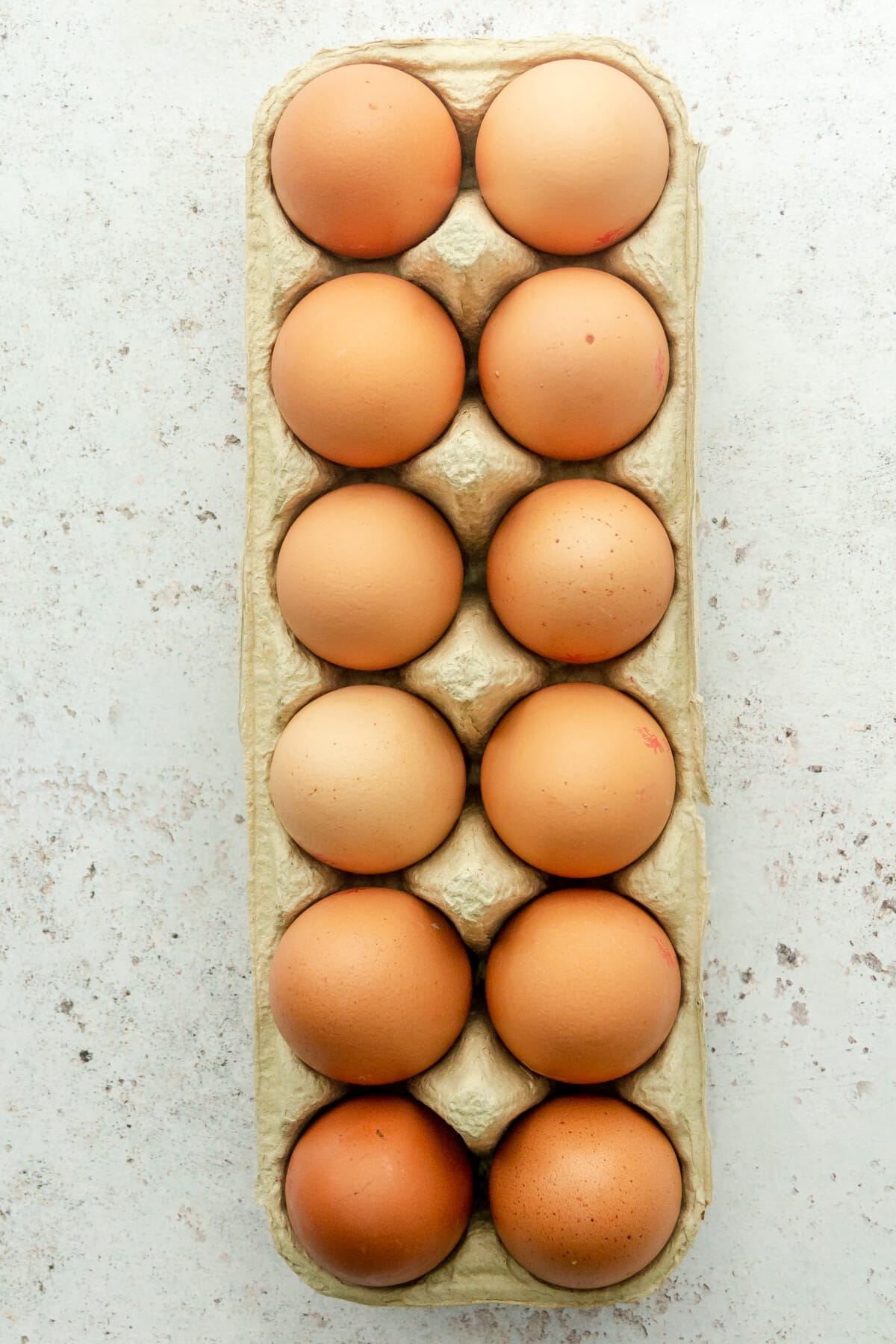 A carton of eggs for perfect hard boiled eggs sit on a light grey surface.