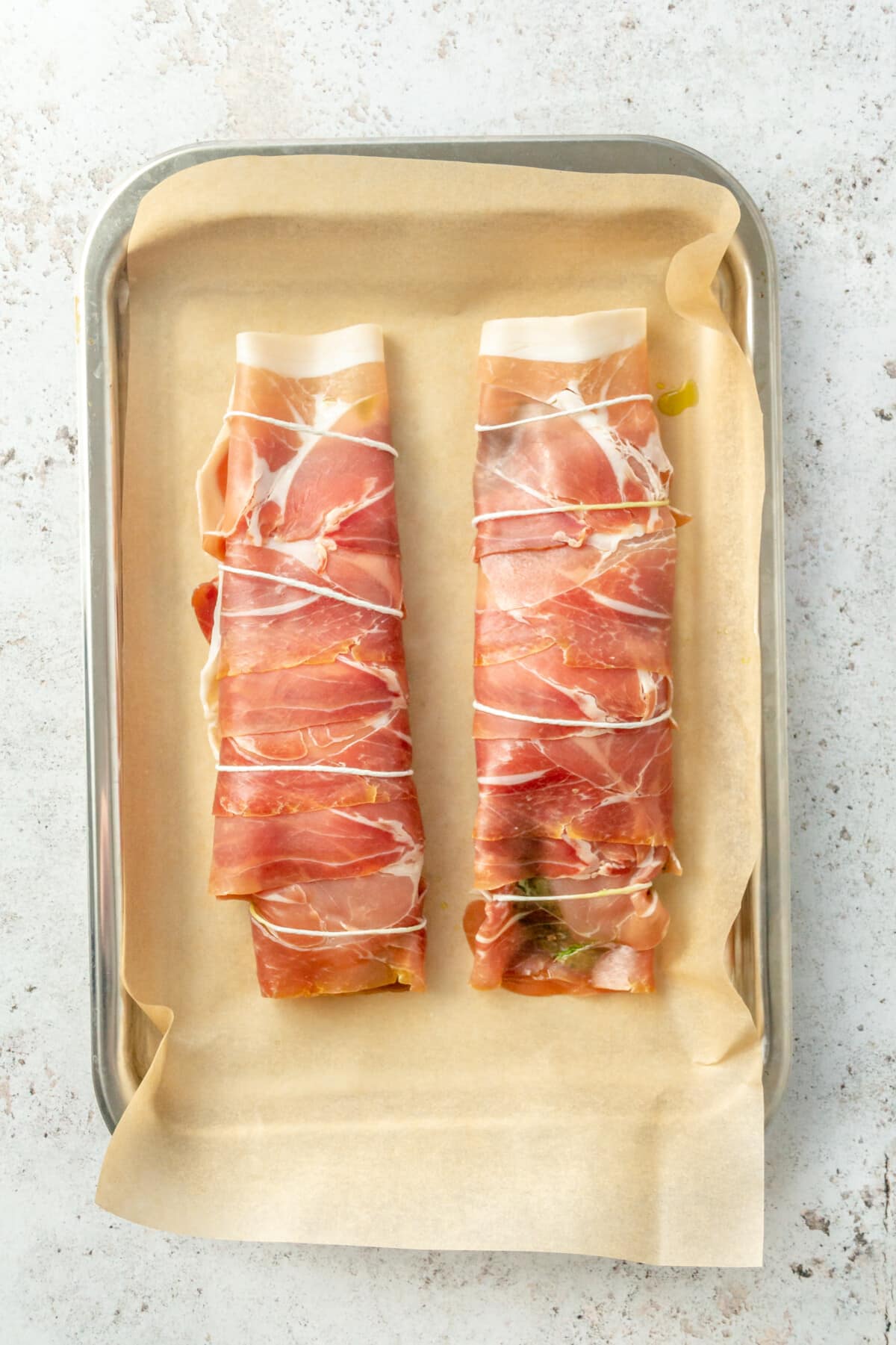 Prosciutto wrapped chicken breasts sit on a parchment lined baking sheet.