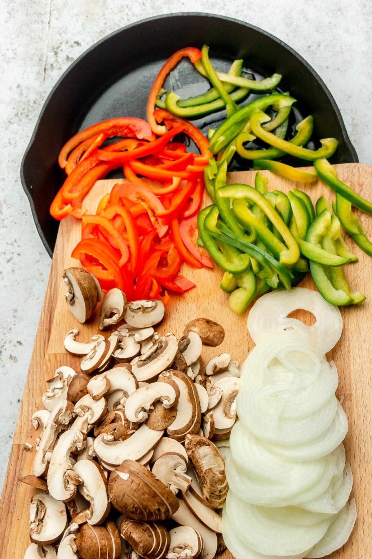 Vegetables are slid into a cast iron skillet from a chopping board sitting on a light grey colored surface.