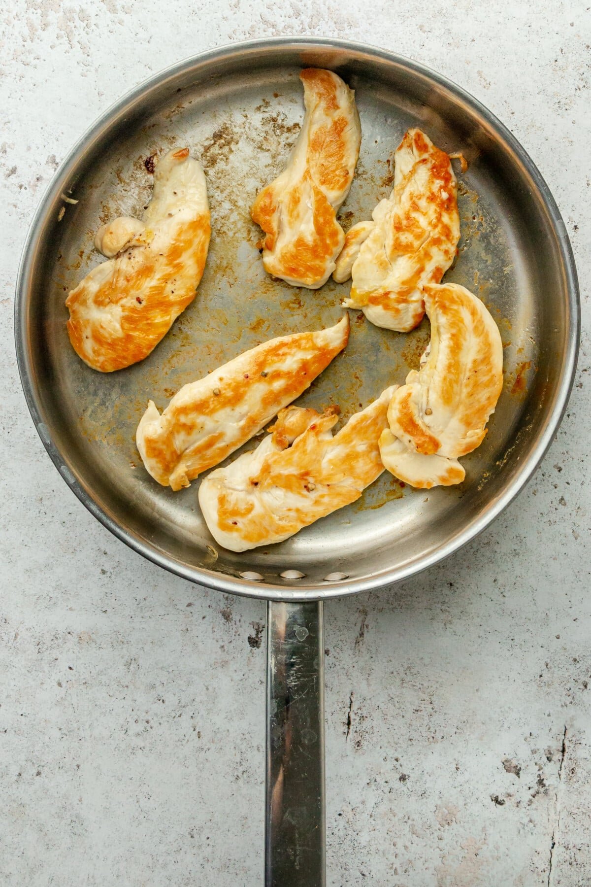 Golden chicken tenders sit in a stainless steel frying pan on a light grey surface.