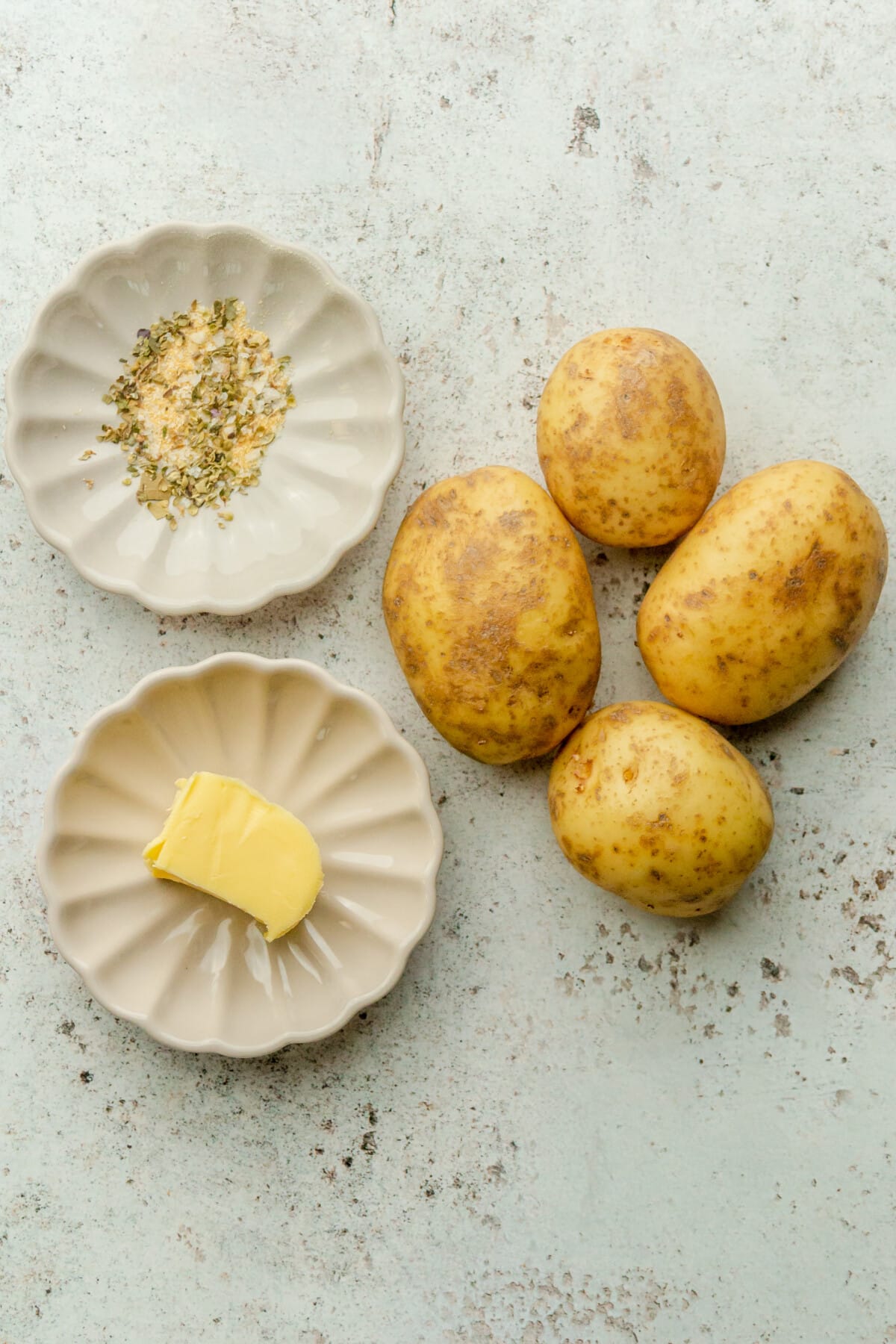 Ingredients for crispy smashed potatoes sit in a variety of plates on a light grey surface.