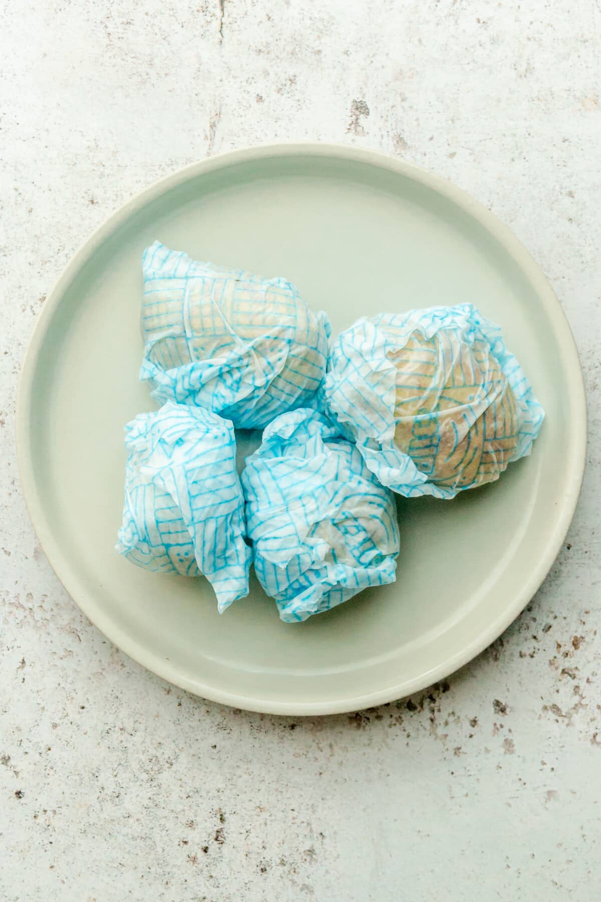 Wet paper towel wrapped potatoes sit on a rimmed ceramic plate on a light gray surface.