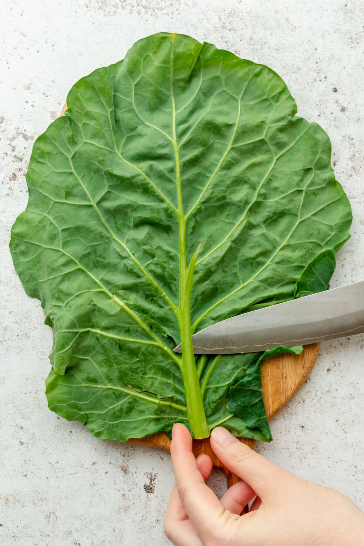 The thickest part of a collard green leaf is shaved on a light grey surface.