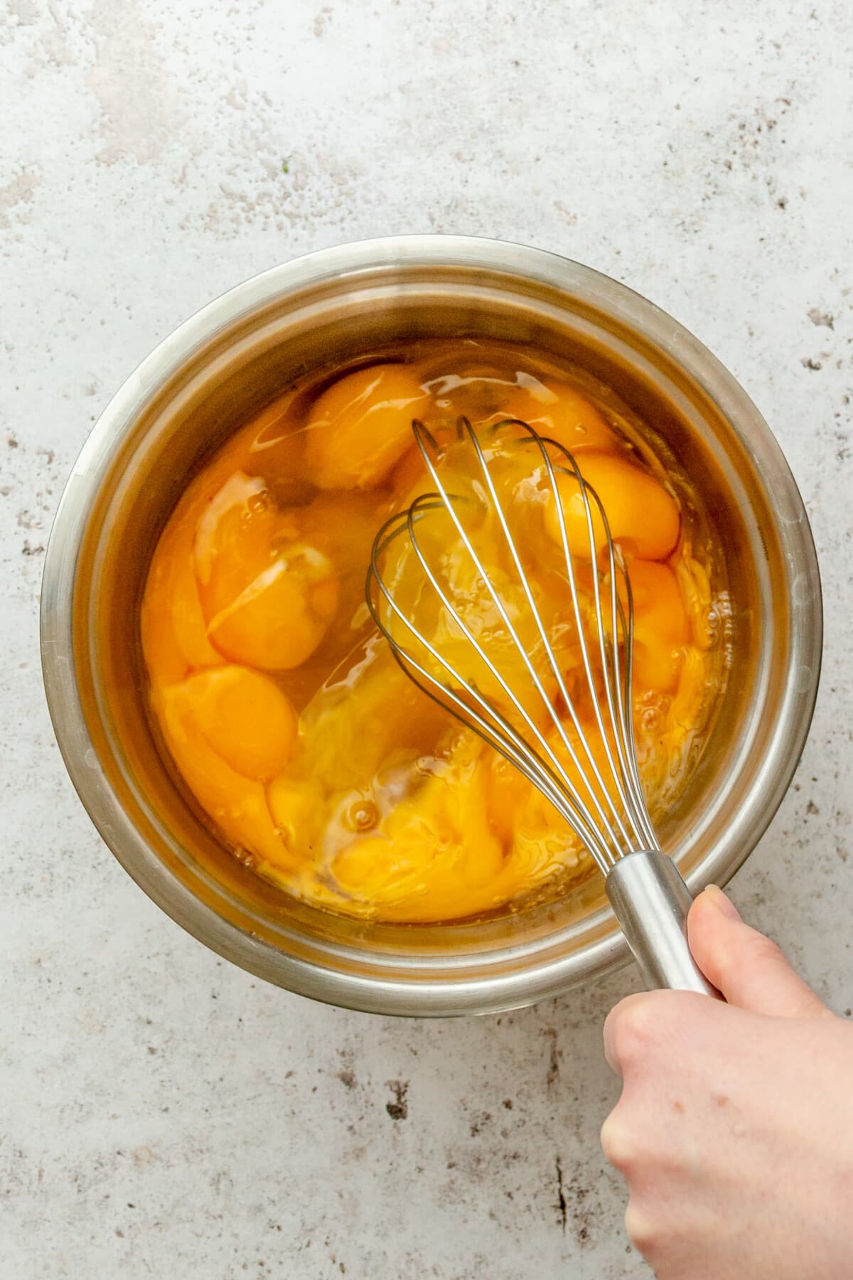 Eggs are whisked in a stainless steel bowl on a light grey surface.