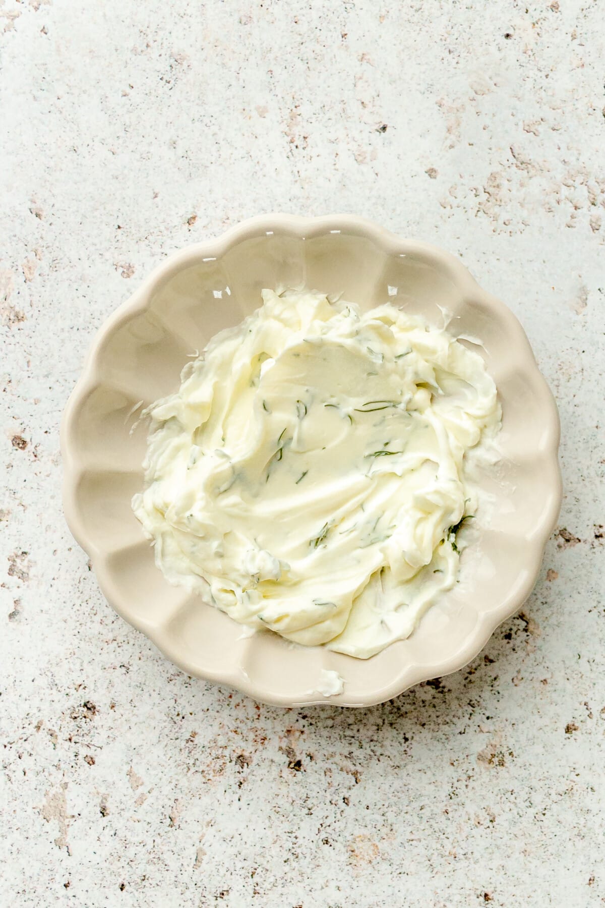 A dill cream cheese mixture sits on a small ceramic plate on a light grey surface.