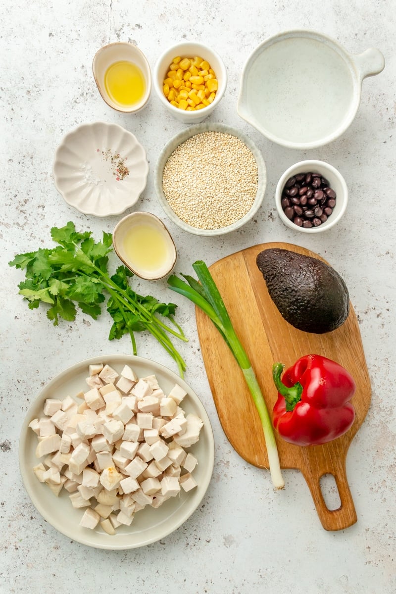 Ingredients for southwestern quinoa salad sit in a variety of bowls on a light grey colored surface.