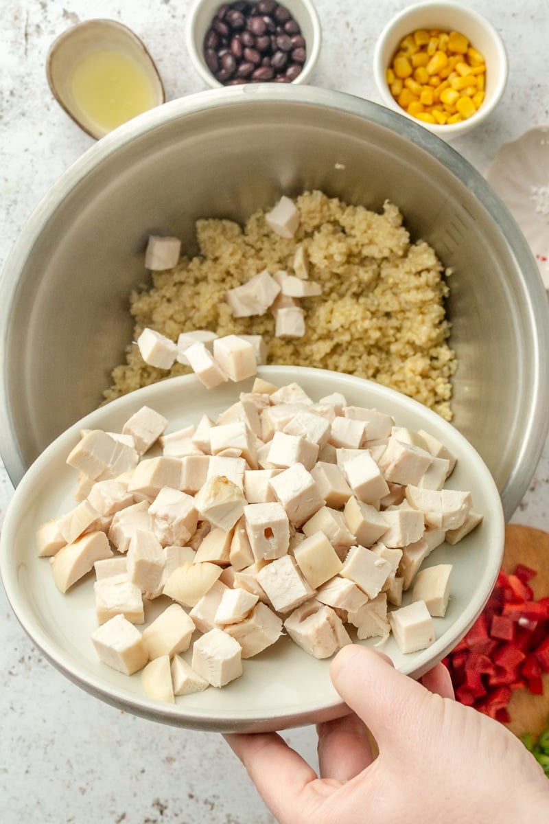 Cubed pieces of chicken are shown being poured over the top of the quinoa.