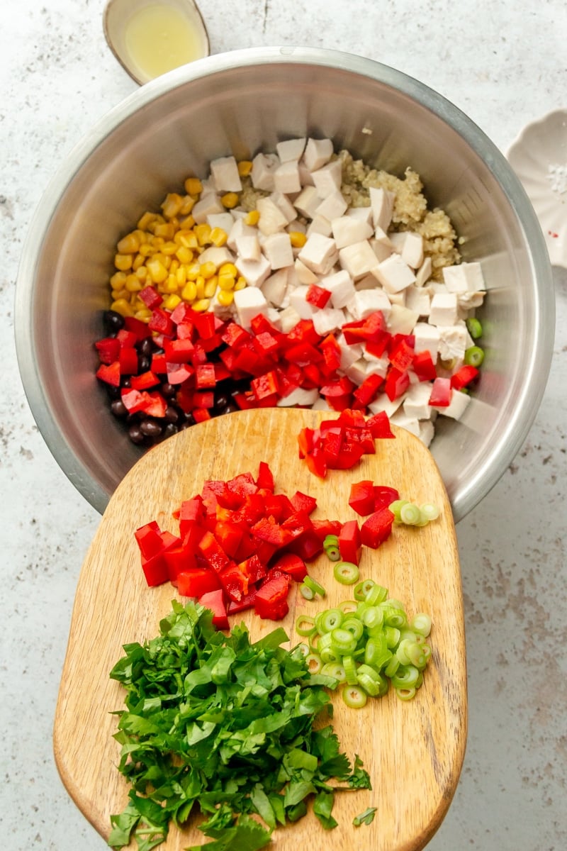 A variety of chopped veggie are shown being poured into a large metal mixing bowl.