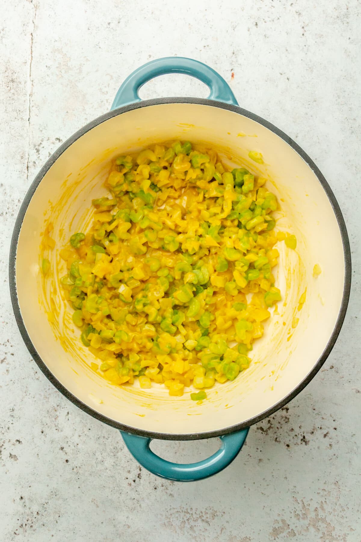 Mustard stirred through chopped vegetables in a Dutch oven on a light gray surface.