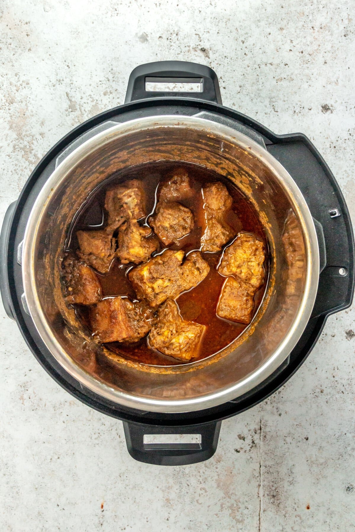 Cooked chunks of marinated pork shoulder sit in an instant pot on a light grey surface.