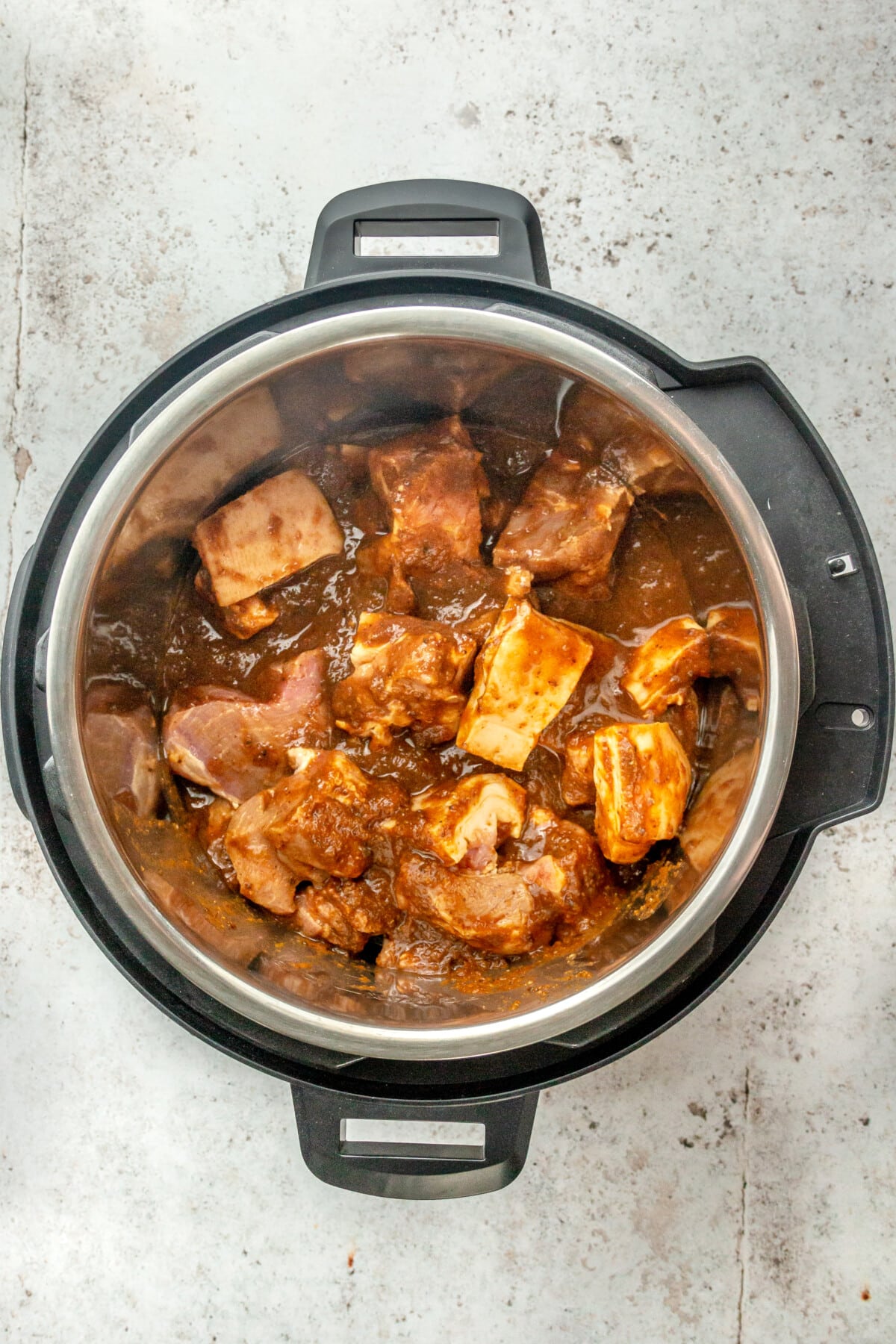 Chunks of marinated pork shoulder sit in an instant pot on a light grey surface.