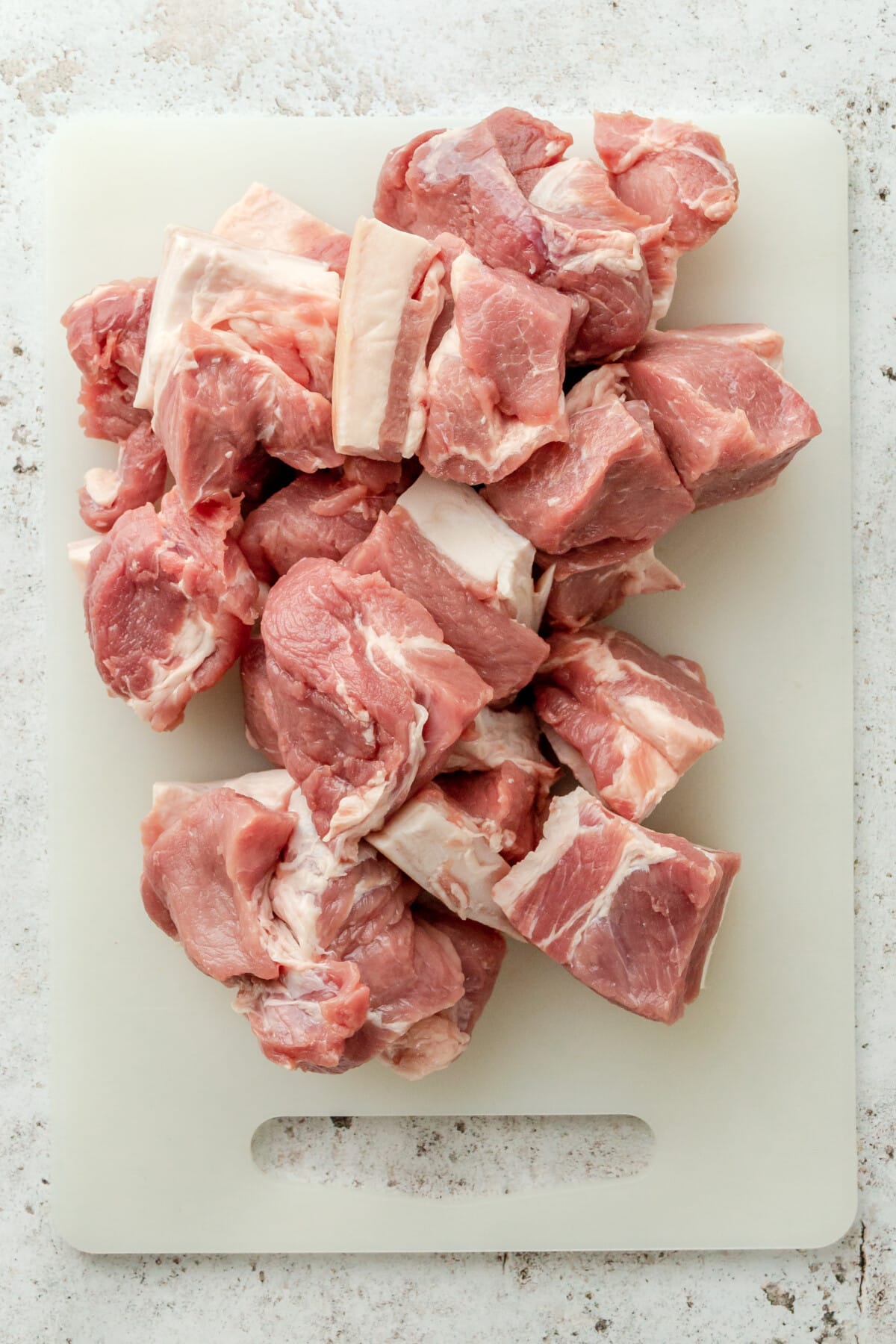 Chunks of pork shoulder sit on a plastic chopping board on a light grey surface.
