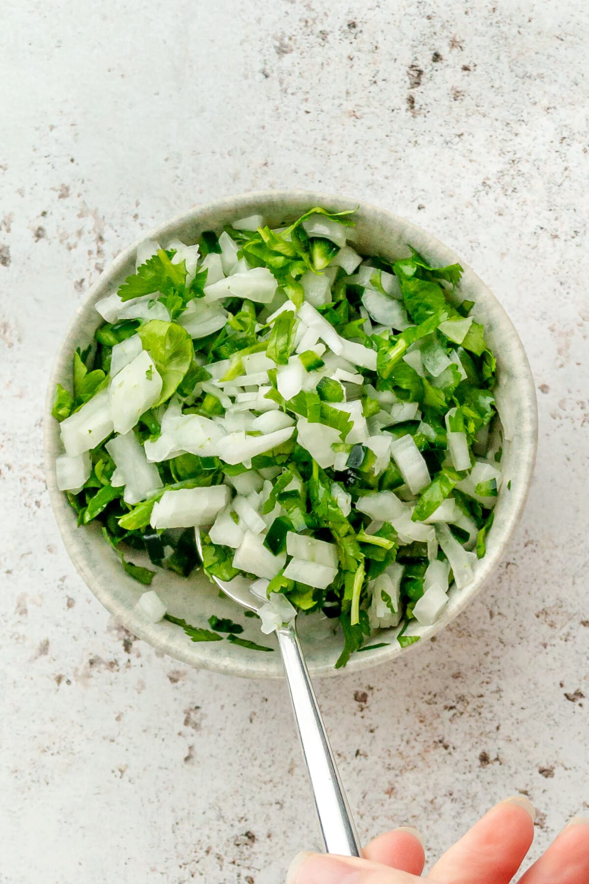 A white onion and cilantro relish is stirred in a small blue ceramic bowl on a light grey surface.