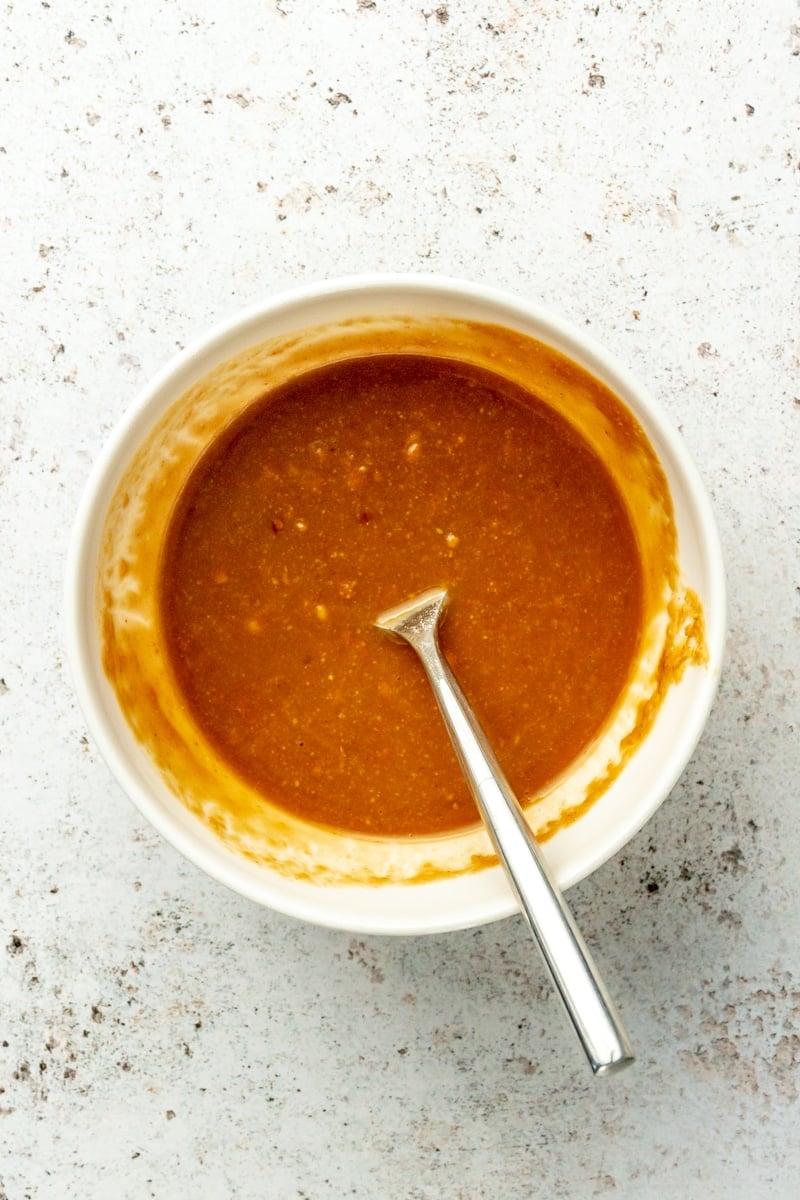 An orange colored saucy mixture sits in a white bowl with a metal spoon.