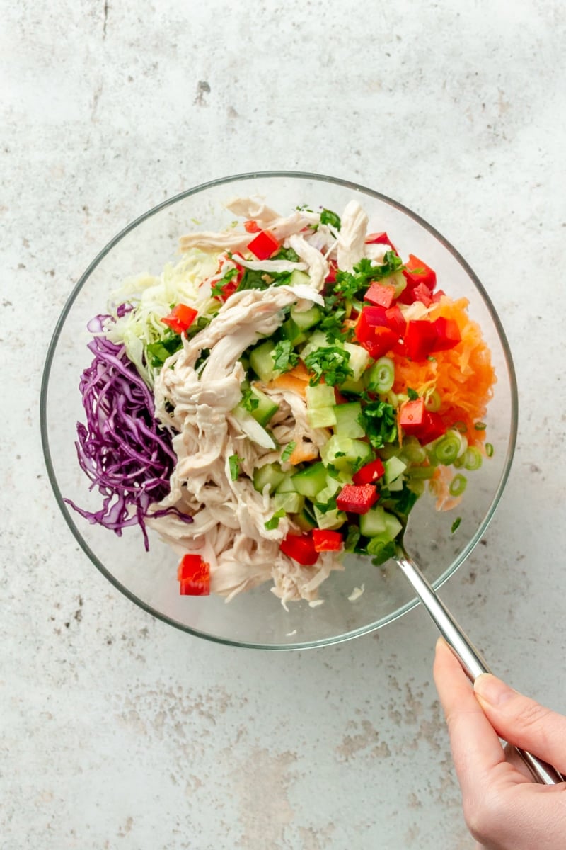 Ingredients for Thai inspired chicken salad are shown being combined in a glass mixing bowl.