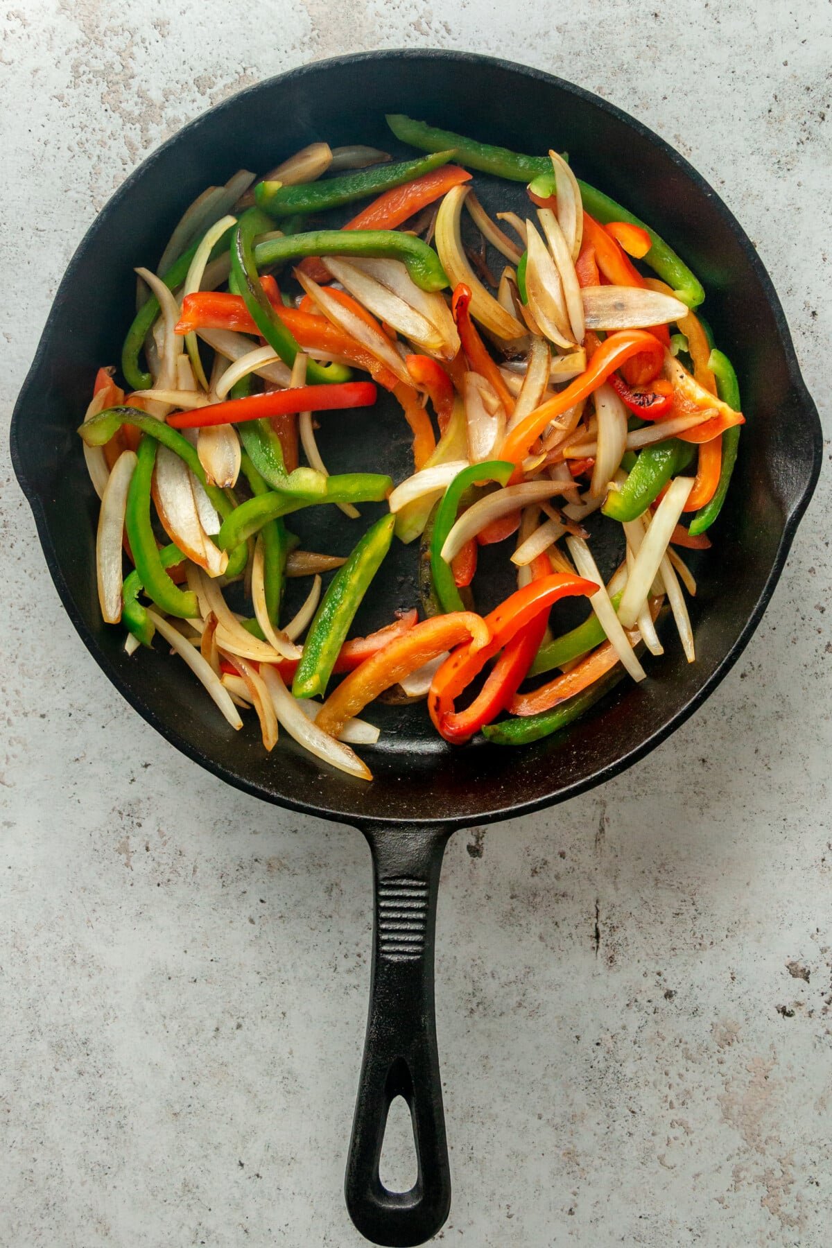 Slices of cooked peppers and onion sit in a cast iron skillet on a light grey surface.