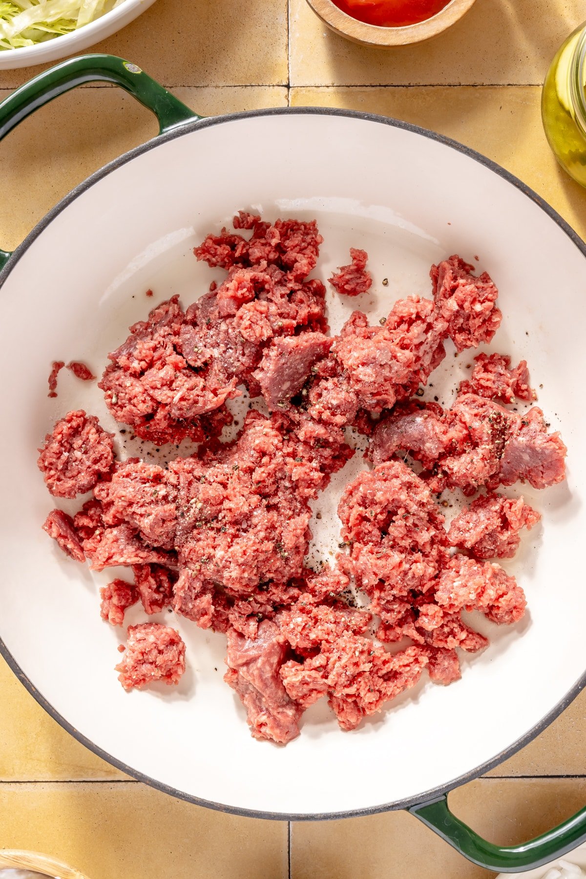 Ground beef cooking in an enameled cast iron skillet.