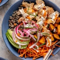 A colorful buffalo chicken bowl topped with pickled onions, avocado, and ranch dressing.