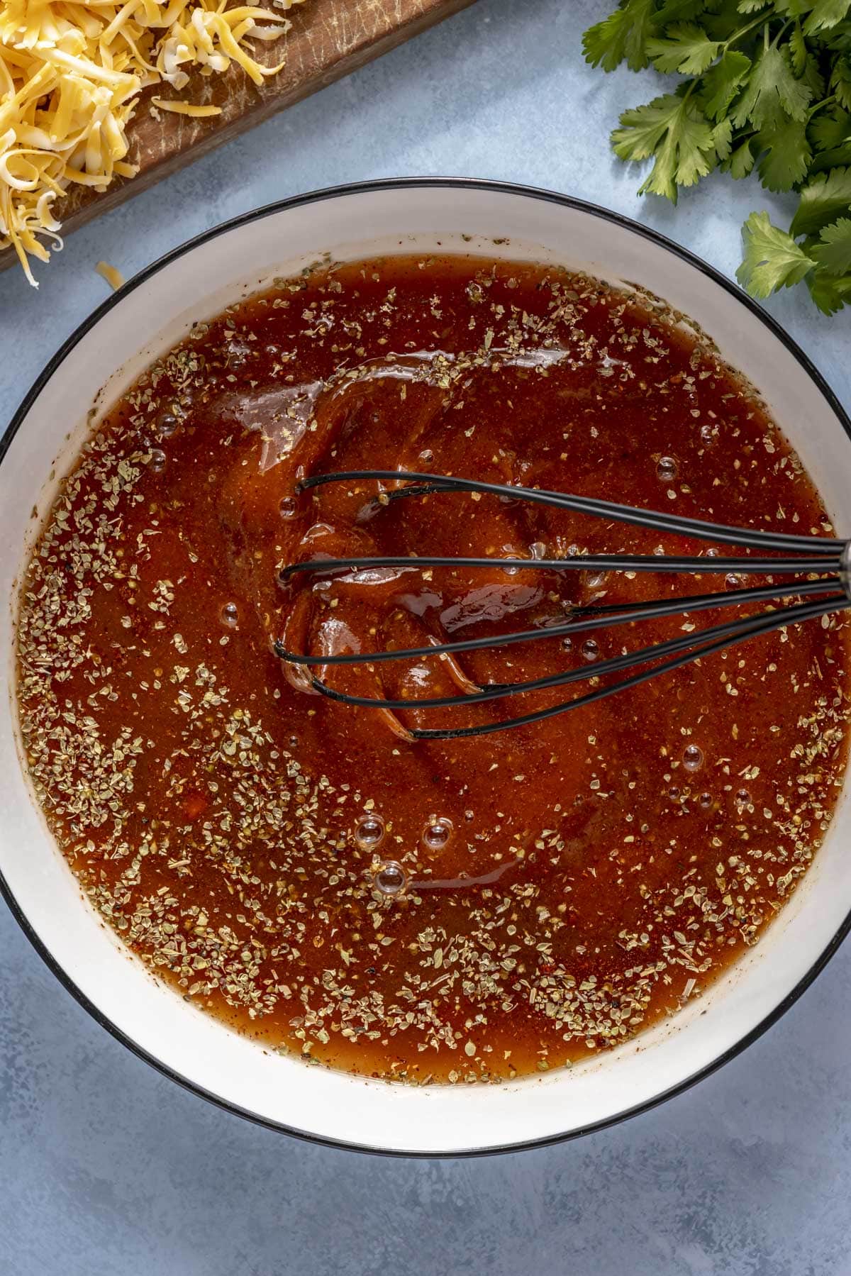A person whisking together homemade enchilada sauce in a small white bowl.