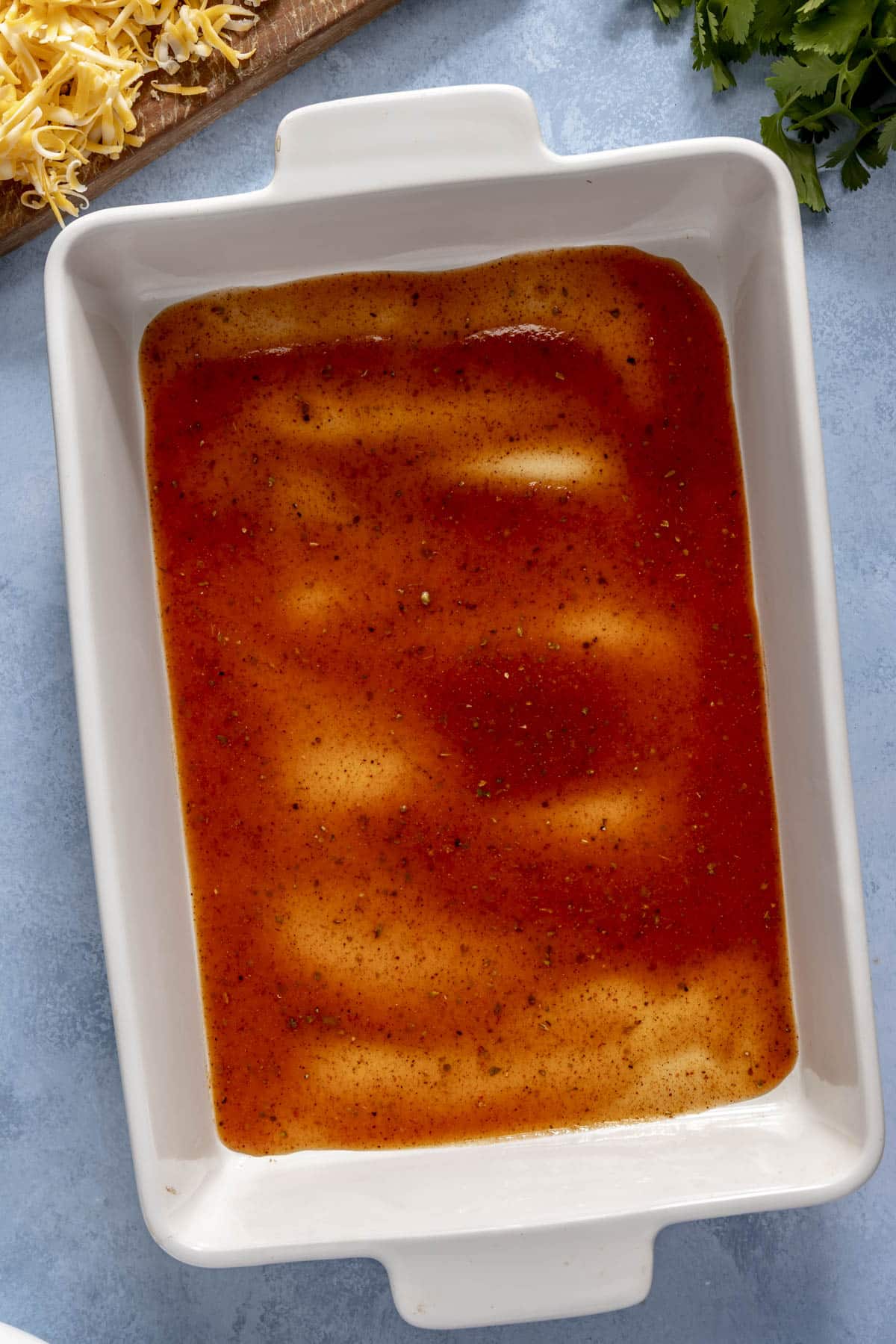 The assembly of a chicken enchilada casserole in a 9x13-inch casserole dish.