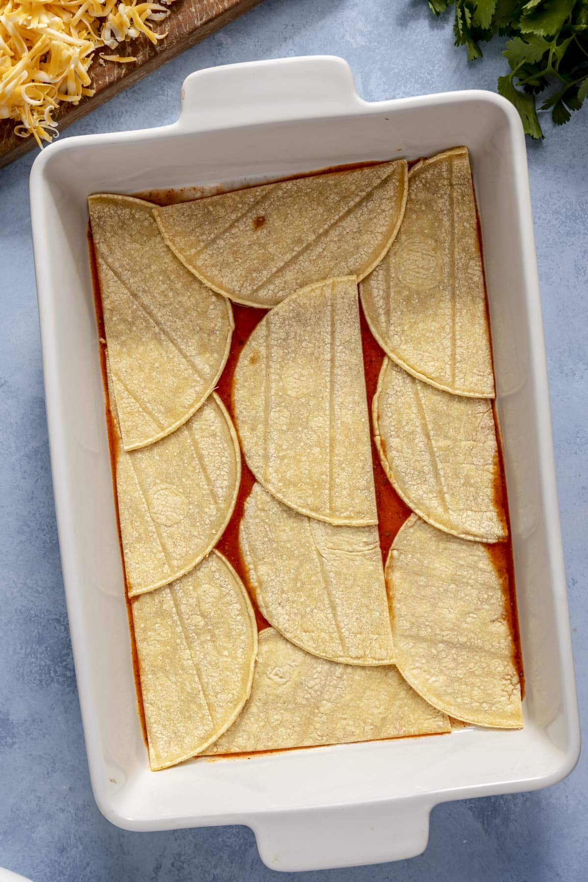 The assembly of a chicken enchilada casserole in a 9x13-inch casserole dish.
