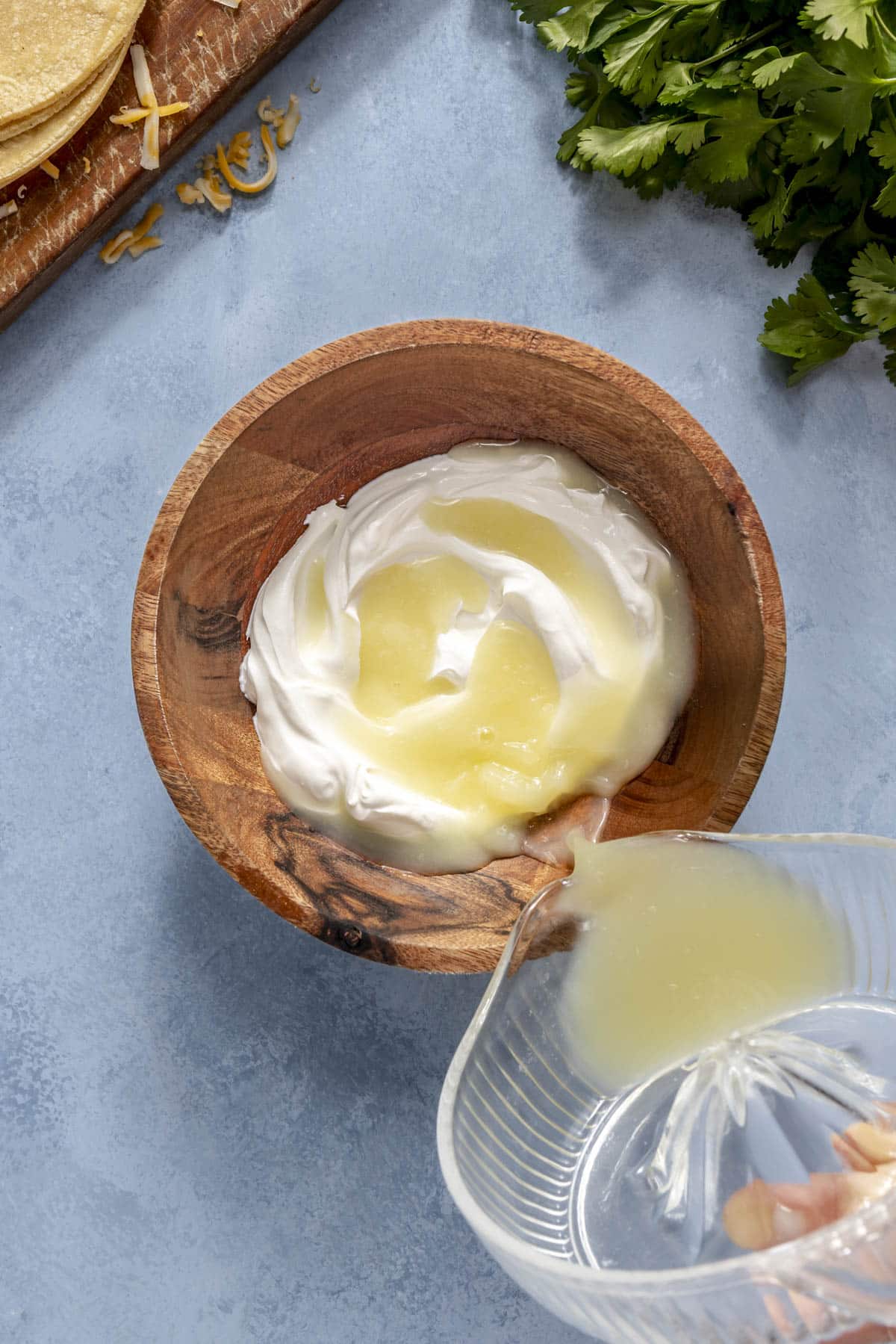 A person adding lime juice to a small bowl of sour cream to make a sauce for chicken enchilada casserole.