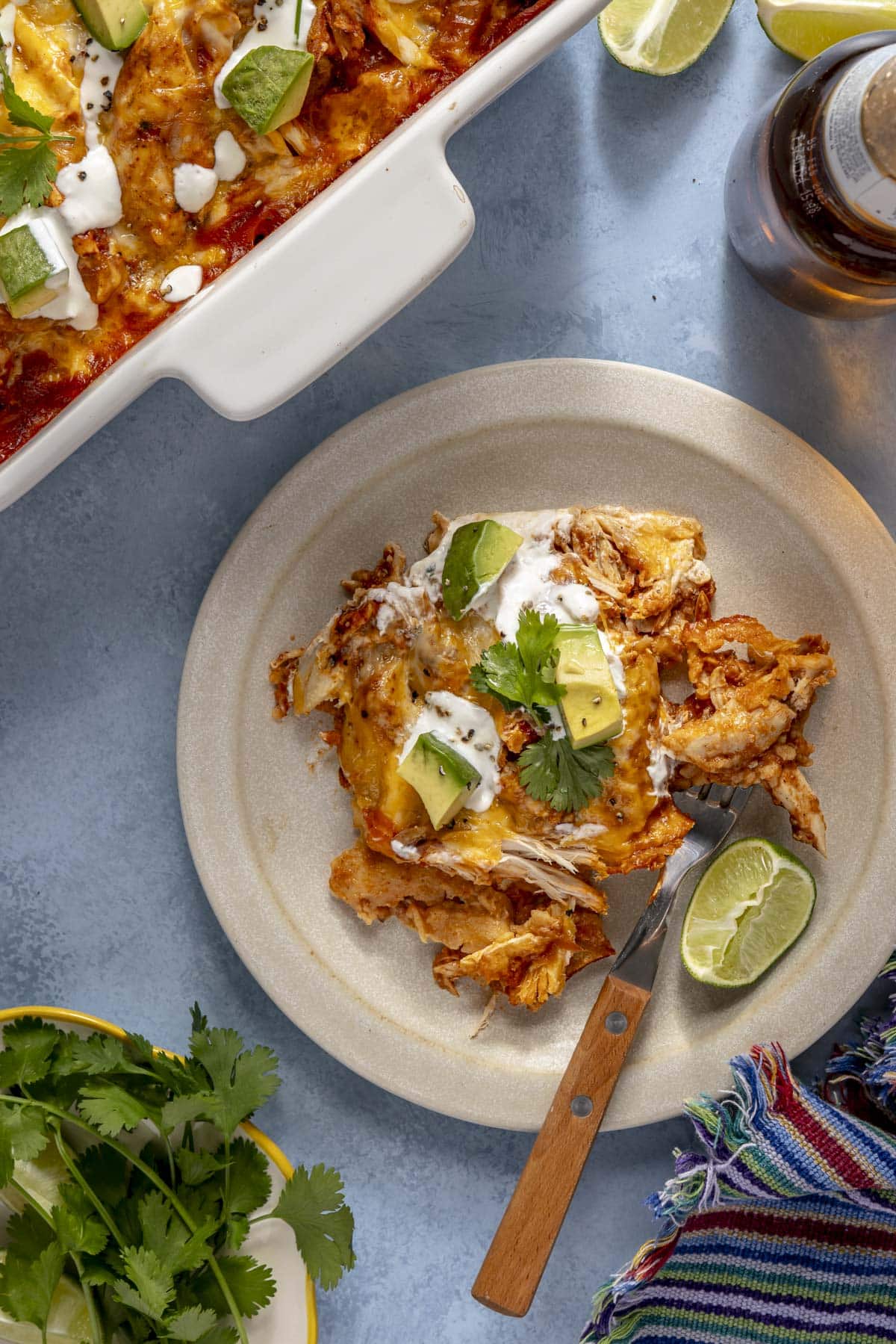 A plate with an individual serving of chicken enchilada casserole on it topped with diced avocados, sour cream, and cilantro.