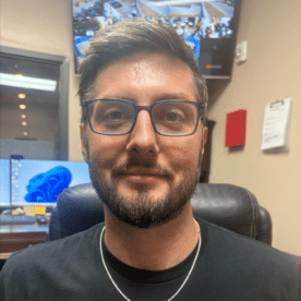 A photo of a man (Michael Hrna) wearing a black MaxxFit t-shirt, smiling at the camera.