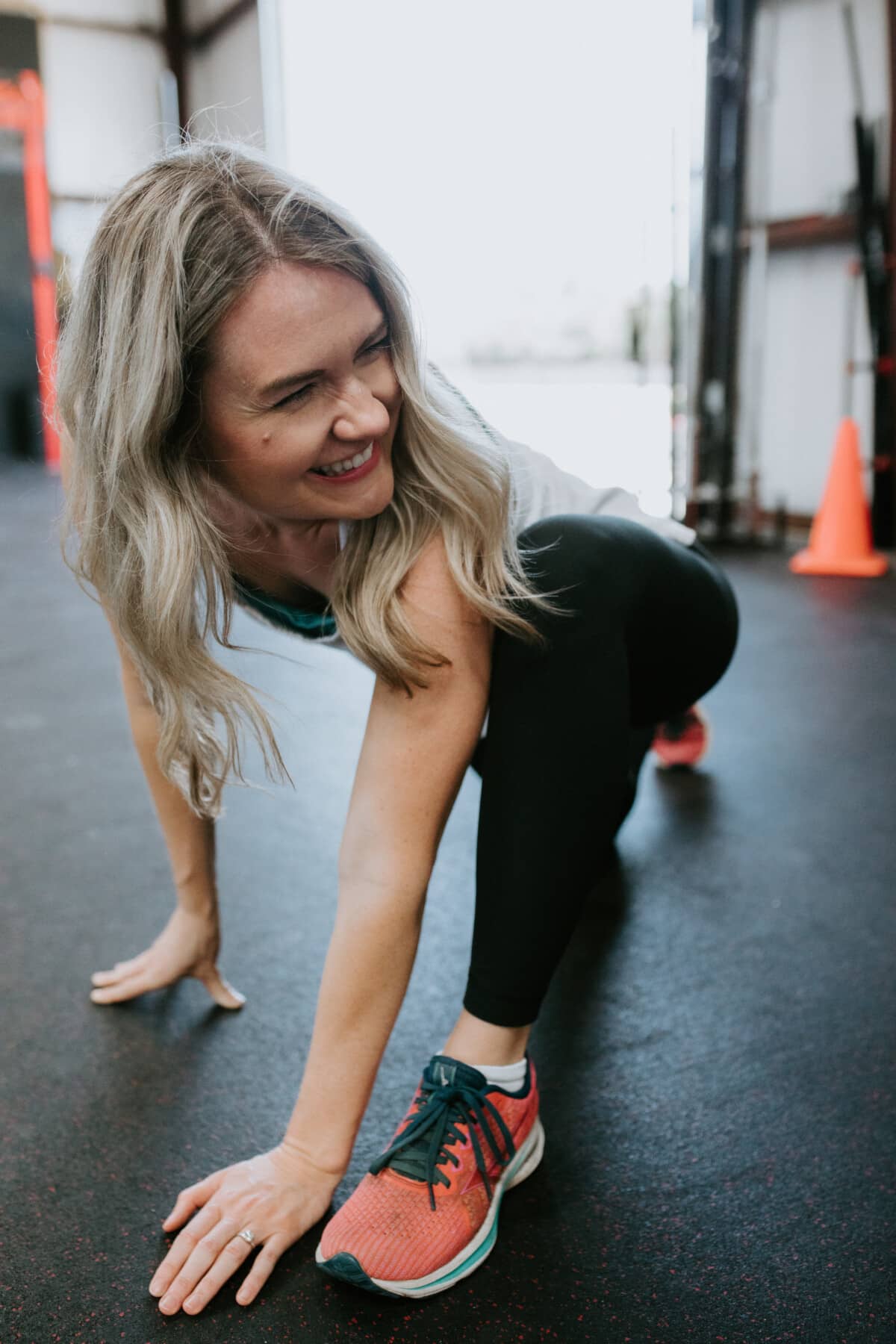 A girl doing a lunge stretch on a black workout mat-style floor.