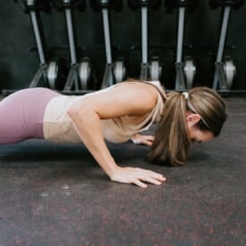 A person wearing exercise clothes and doing a push up on a black workout mat.