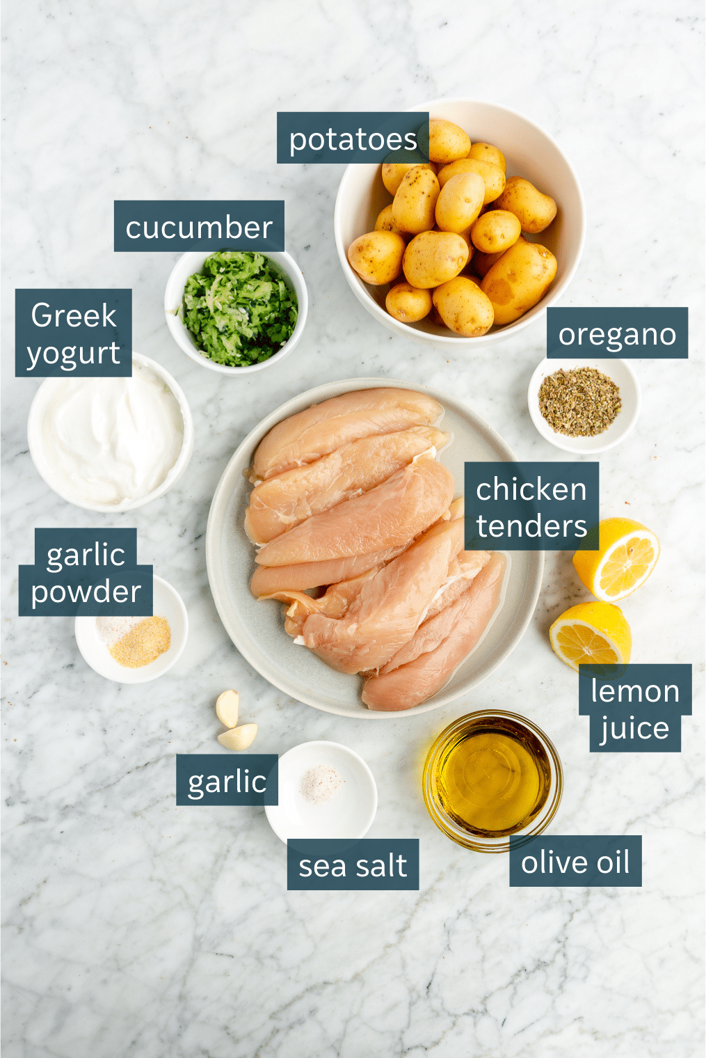 All of the ingredients for a Greek chicken and potato sheet pan dinner on a marble surface.