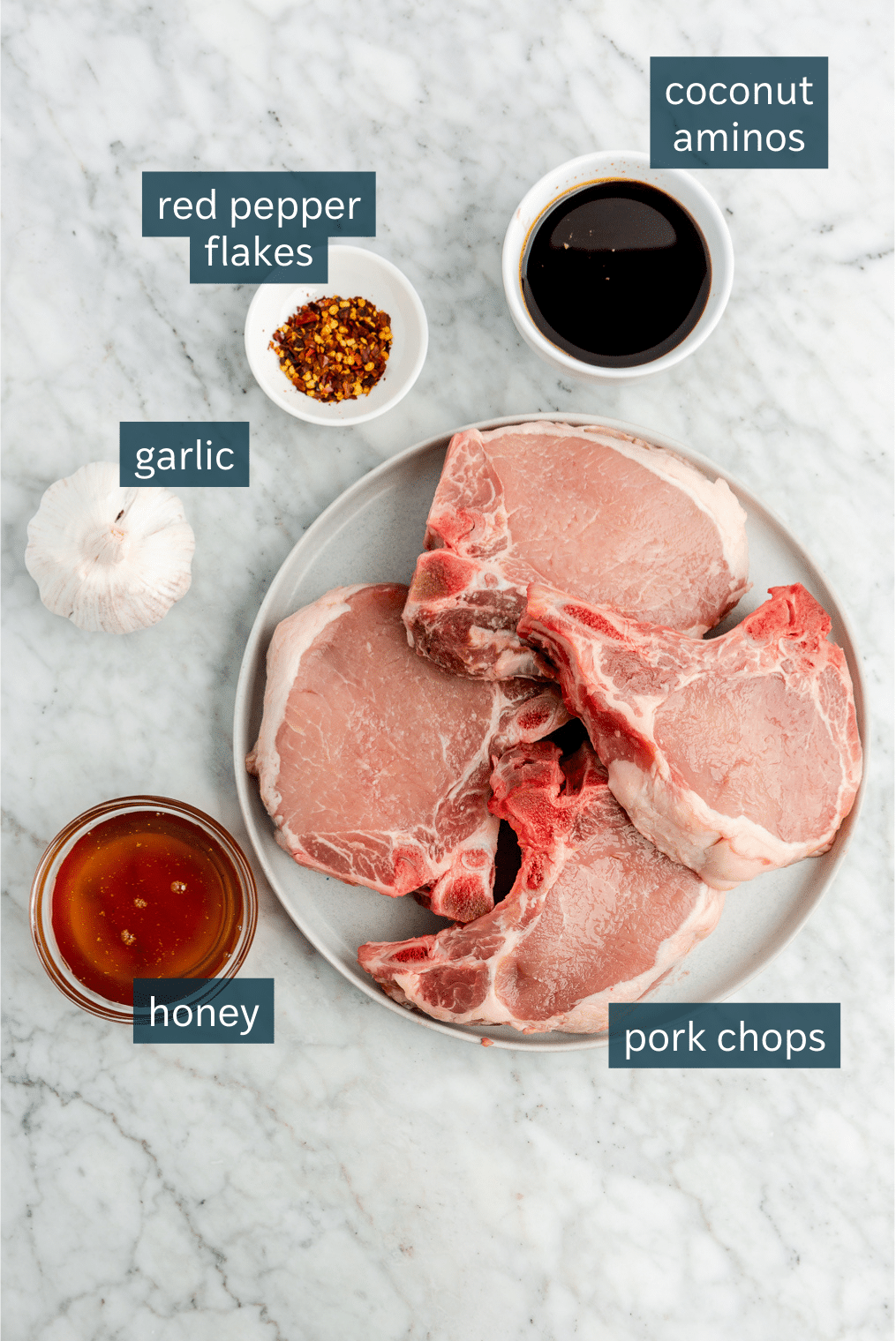 All of the ingredients needed for honey garlic pork chops in different sized bowls on a marble surface.