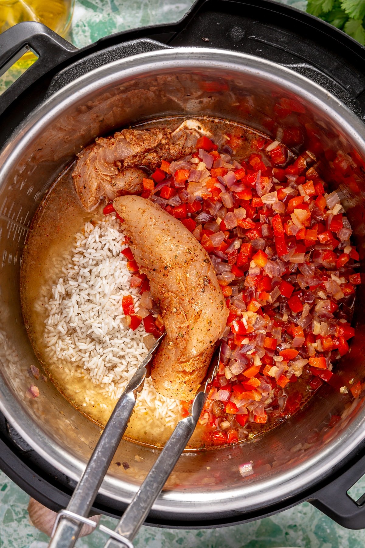 Cooked bell peppers and onions in an Instant Pot alongside chicken broth, uncooked rice, and uncooked fajita seasoned chicken tenders.