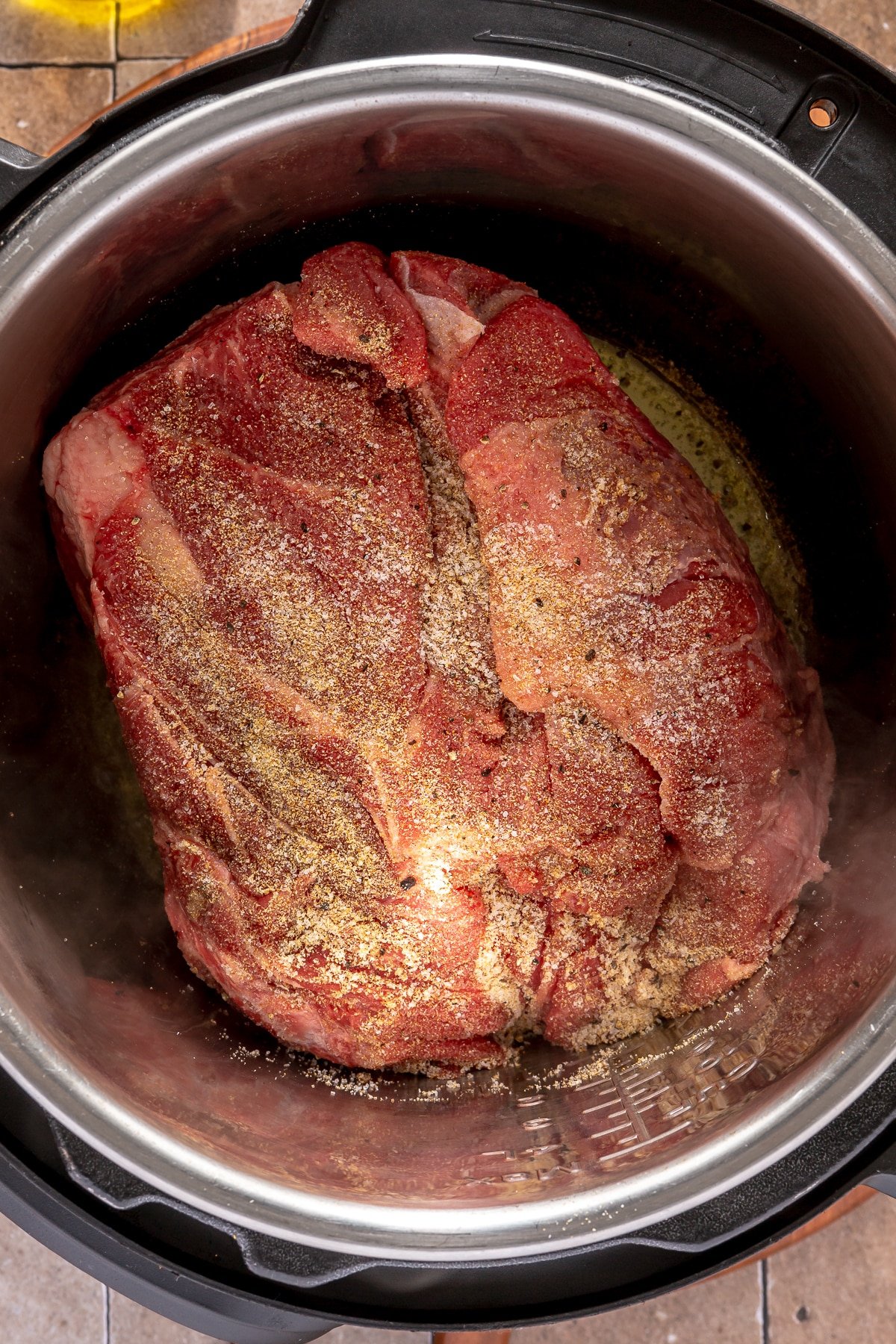 A large, seasoned chuck roast uncooked in an Instant Pot. 