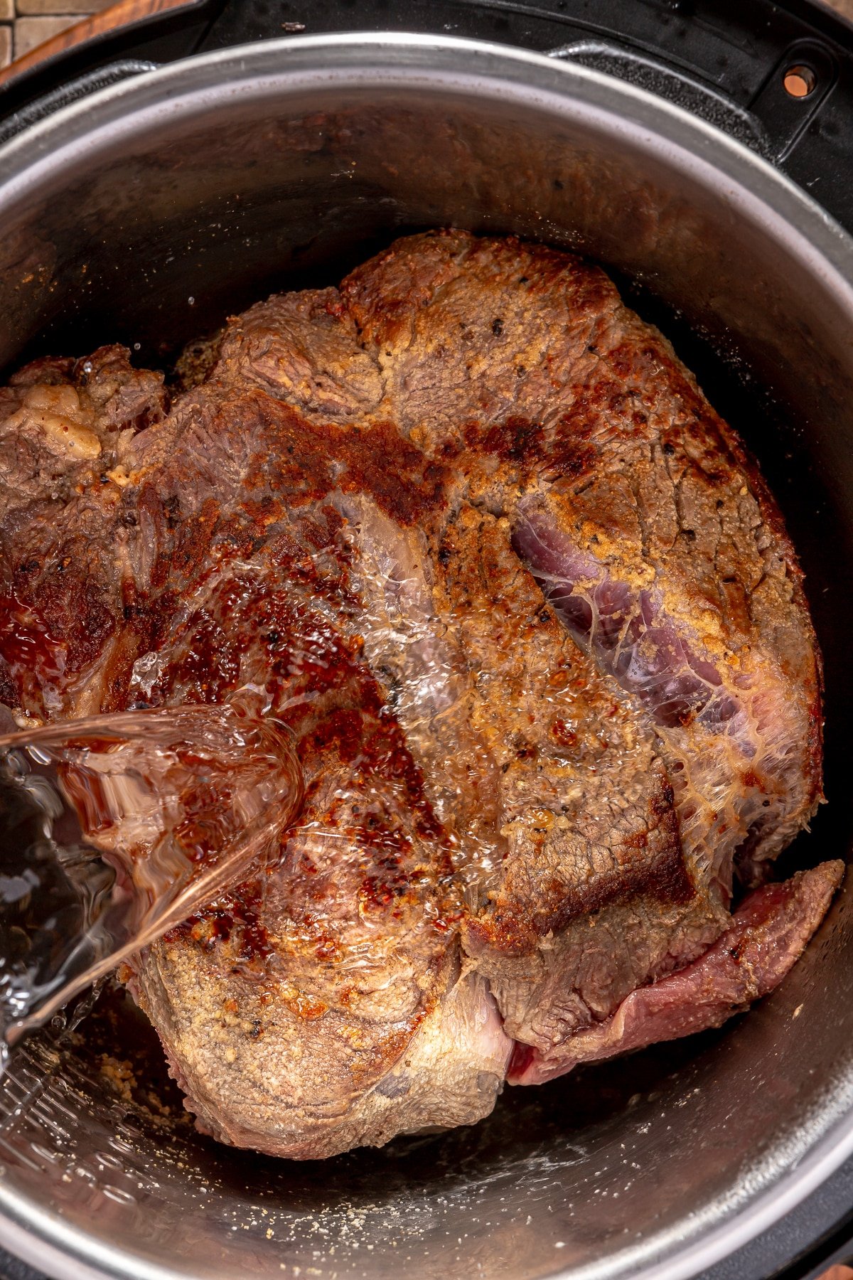 Someone pouring water over a large seared chuck roast in an Instant Pot.