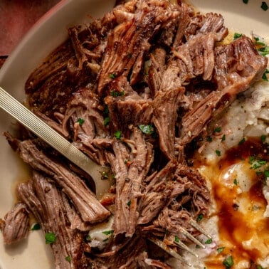 A plate with shredded pot roast and mashed potatoes.