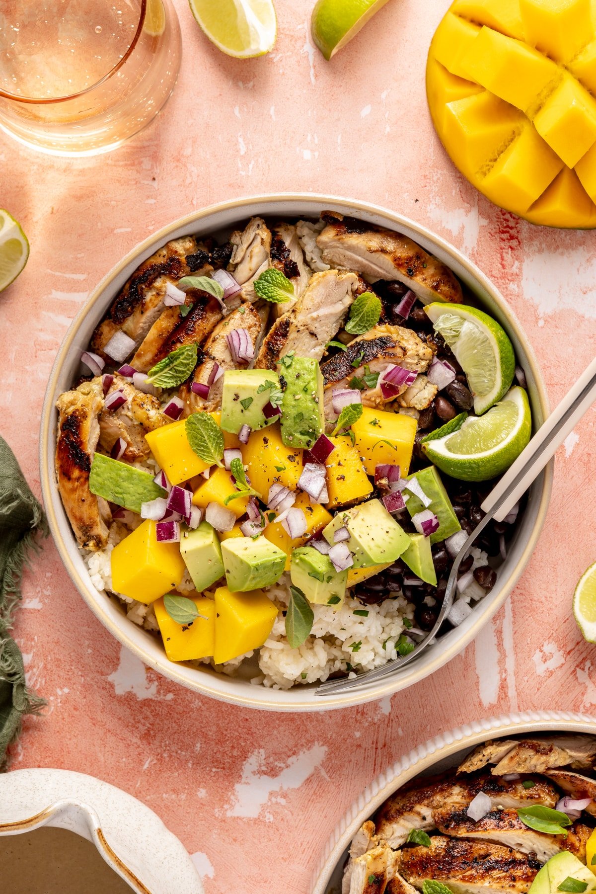 Mojo chicken bowls loaded with rice, beans, chicken, fresh mango, avocado, mint leaves, oregano leaves, and lime wedges.