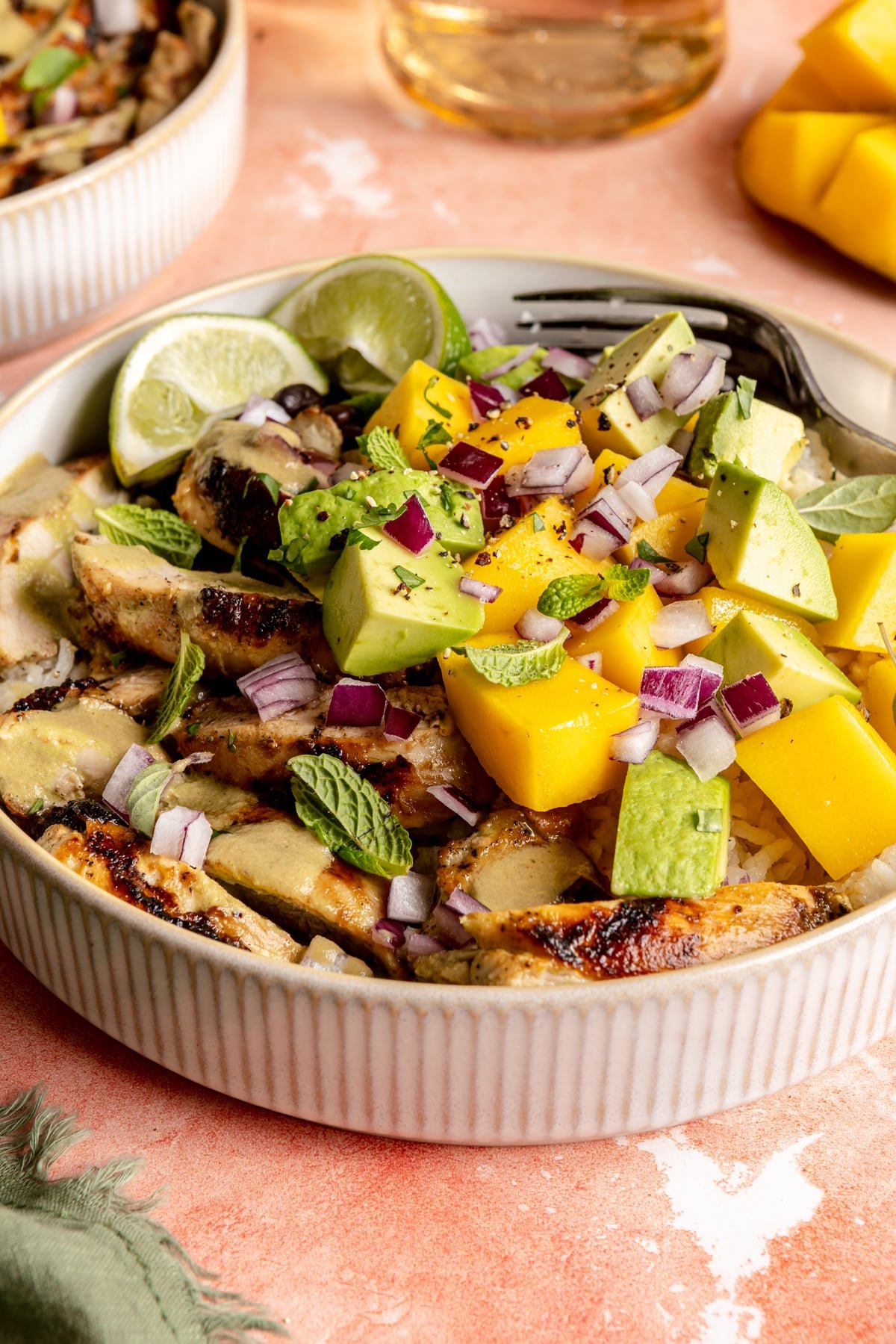 Mojo chicken bowls loaded with rice, beans, chicken, fresh mango, avocado, mint leaves, oregano leaves, and lime wedges.