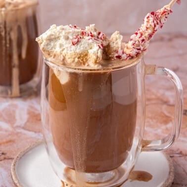 A peppermint mocha latte in a clear glass mug topped with whipped cream and a peppermint stick.