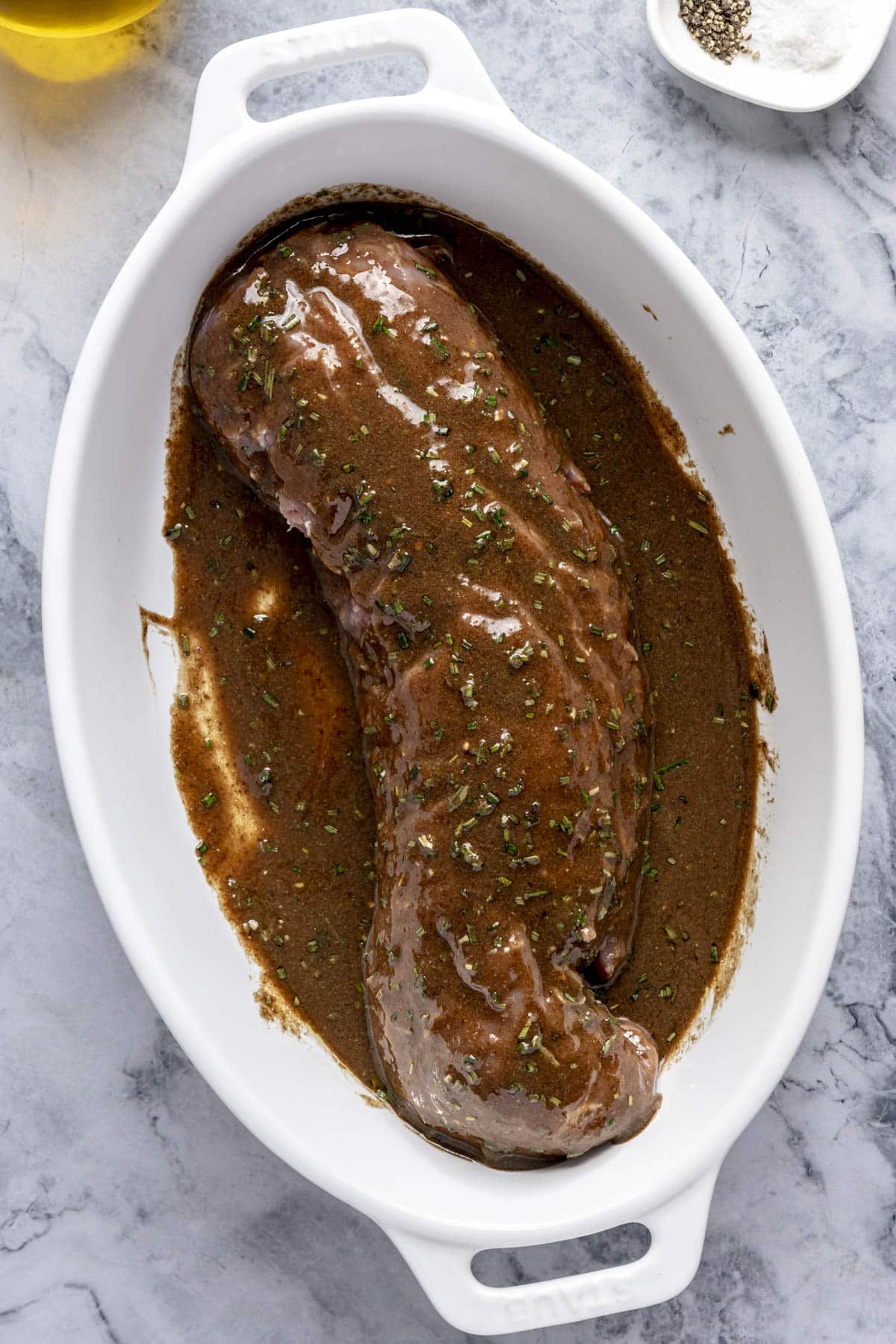 A pork tenderloin marinating in a white baking dish.