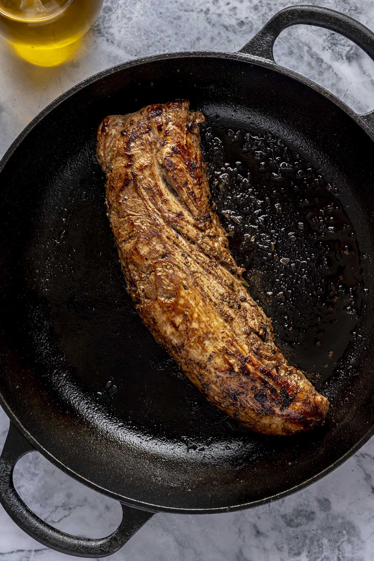 A marinated pork tenderloin searing in a large cast iron pan.