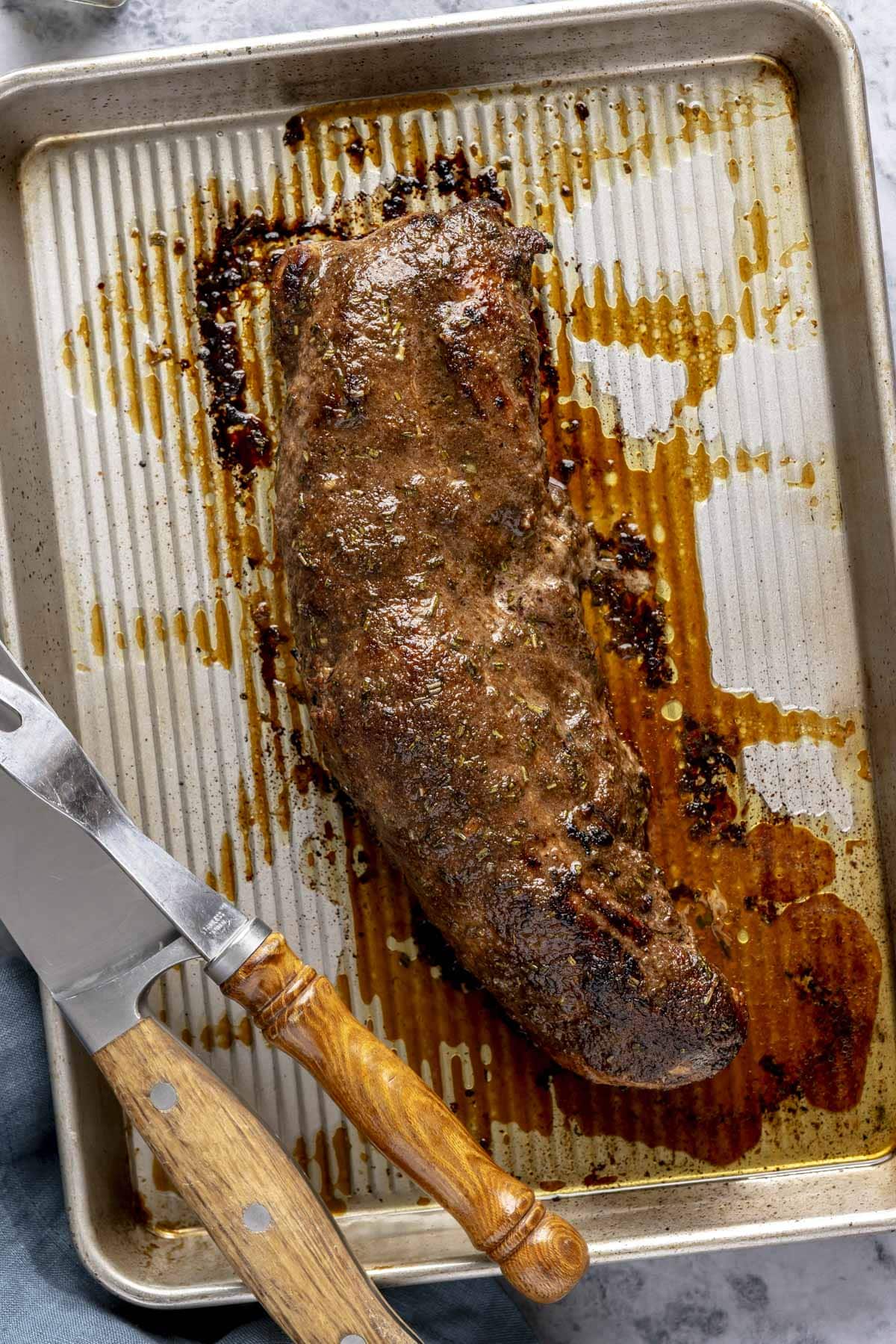 A sheet pan with a marinated and roasted pork tenderloin on it.