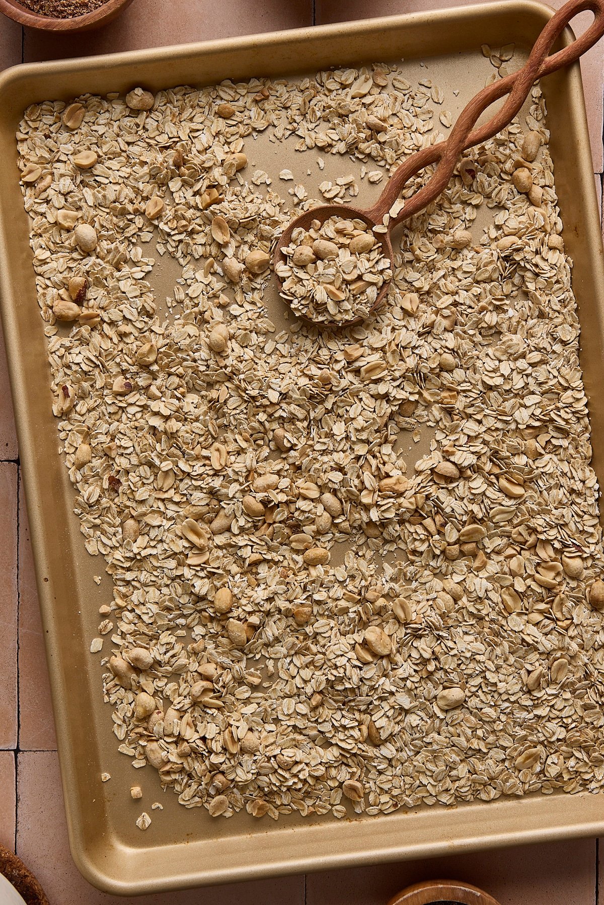 Oats and peanuts on a baking sheet before being toasted in the oven.