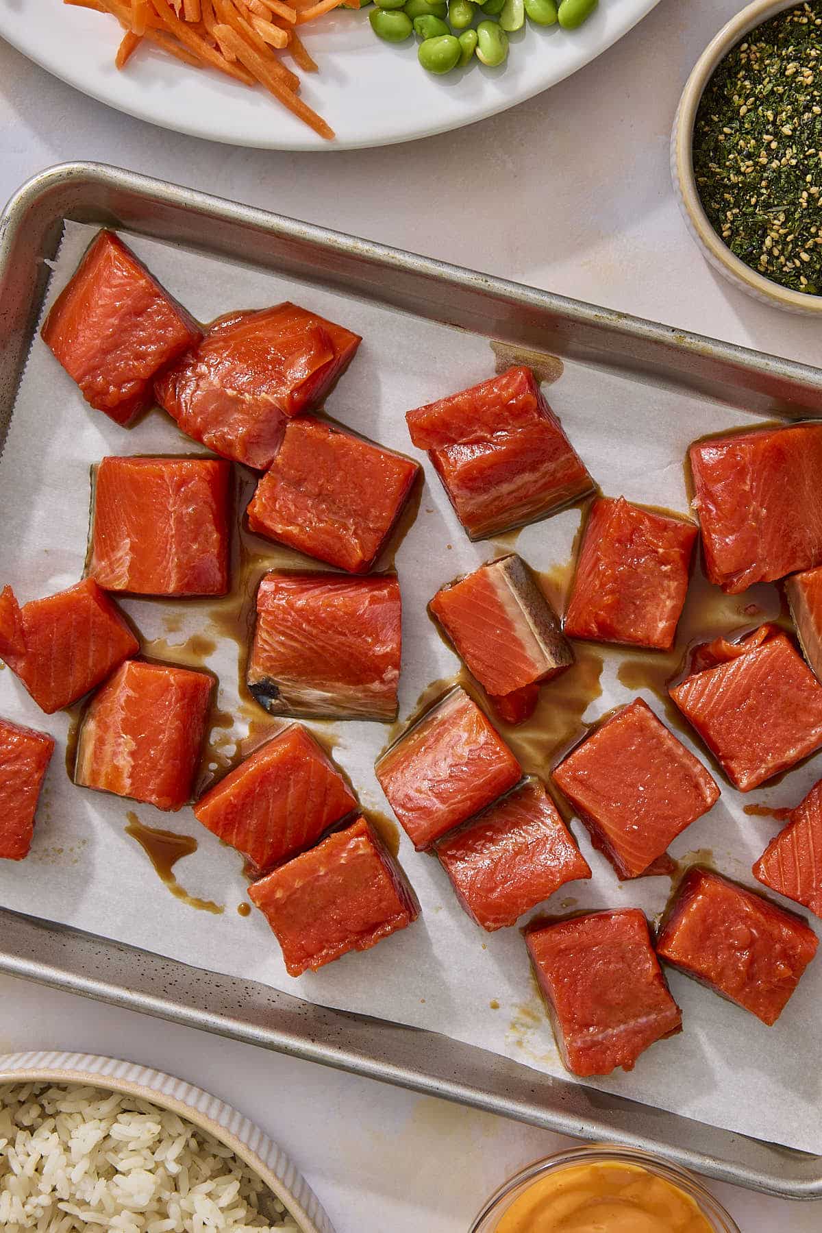 Diced salmon fillet tossed in teriyaki sauce and spread out on parchment paper lined sheet pan.