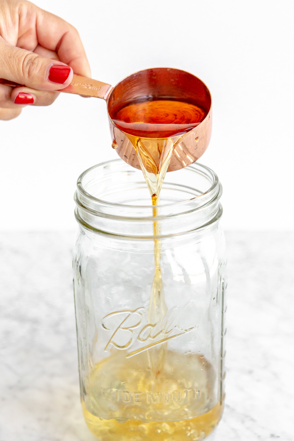 Grand Marnier being poured out of a copper measuring cup into a mason jar.