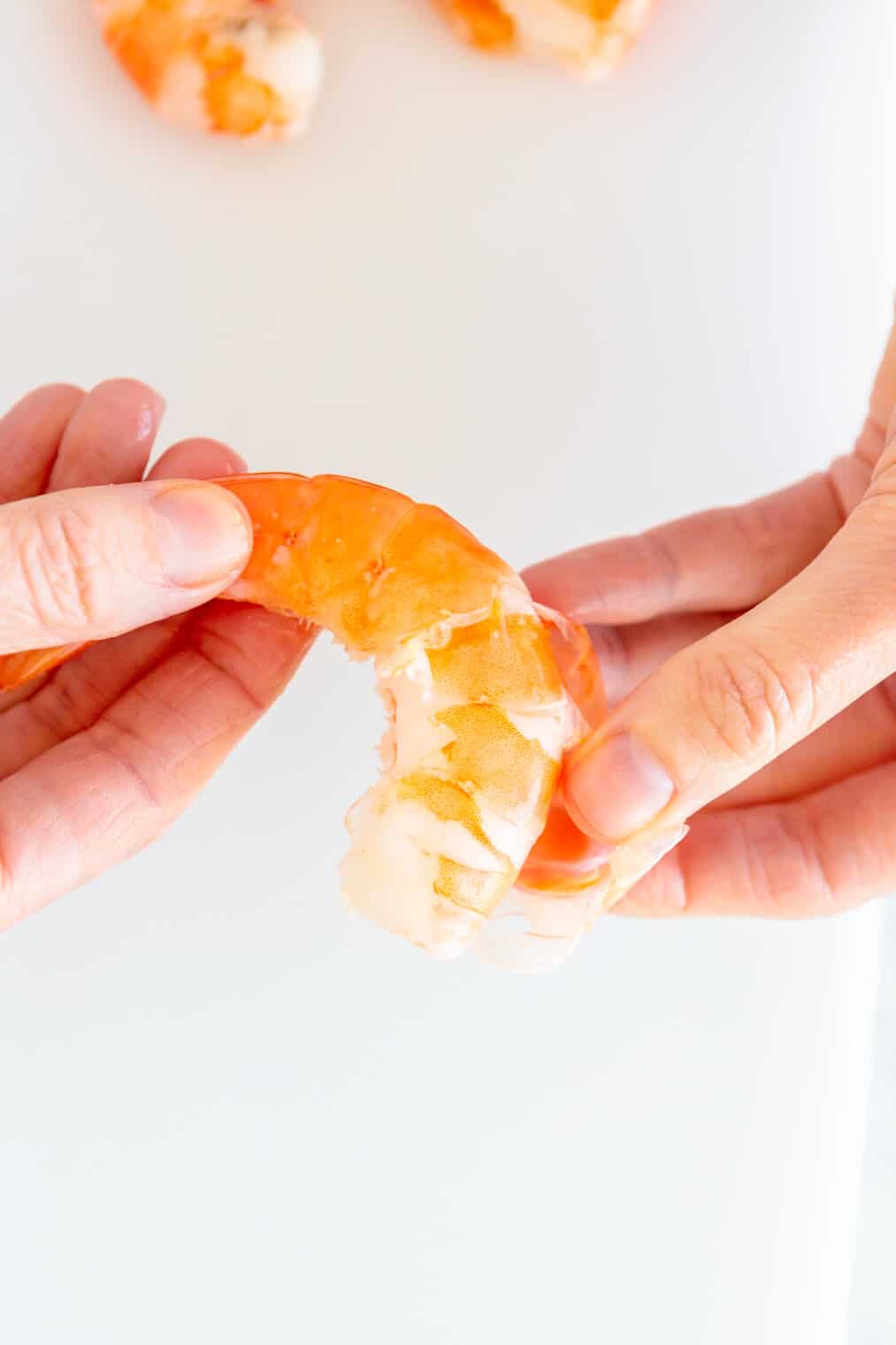 Two hands peeling cooked shrimp.