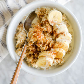 White bowl with cooked oatmeal topped with sliced banana.