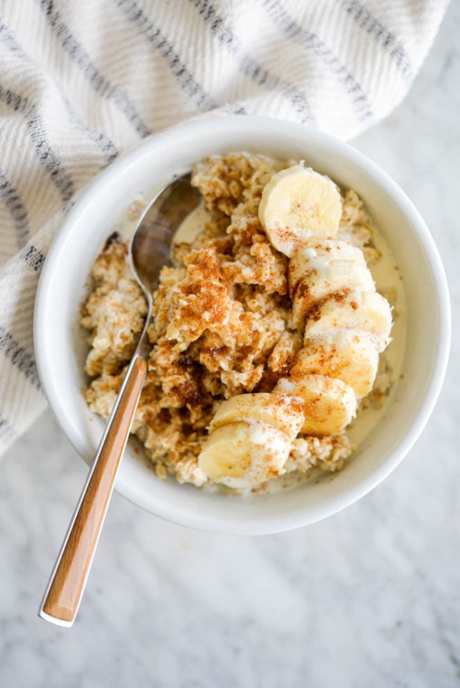 White bowl with cooked oatmeal topped with sliced banana.