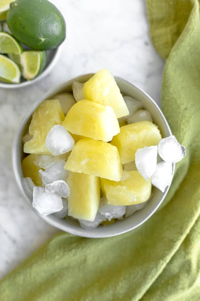 Frozen margarita mix cubes in a bowl with ice cubes and a side dish of limes.